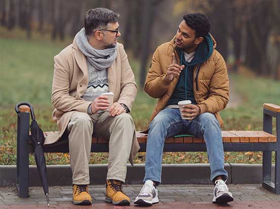 Two men talking on bench outside with a coffee