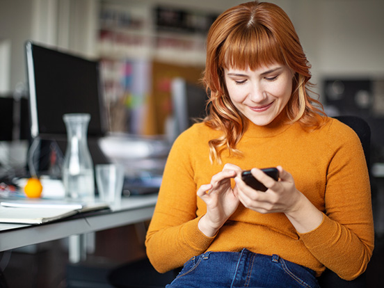 Woman scrolling on phone whilst at office desk