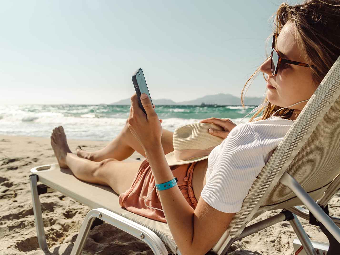 Woman sunbathing on beach with smart phone