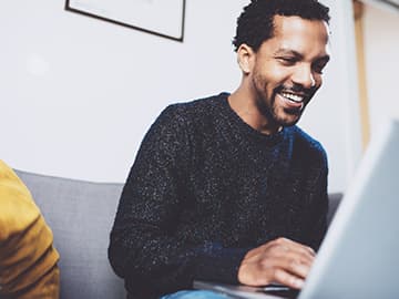 Man smiling using laptop on sofa