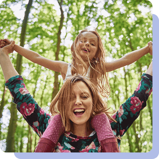 Mother carrying child on her shoulders amongst trees