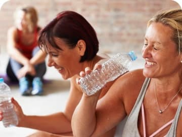 Two women smiling and drinking water at an exercise class
