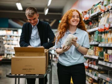 Two grocery store employees smiling whilst re-stocking shelves