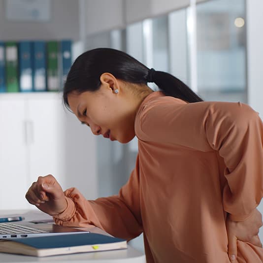 Woman sat in a office holding her lower back in pain