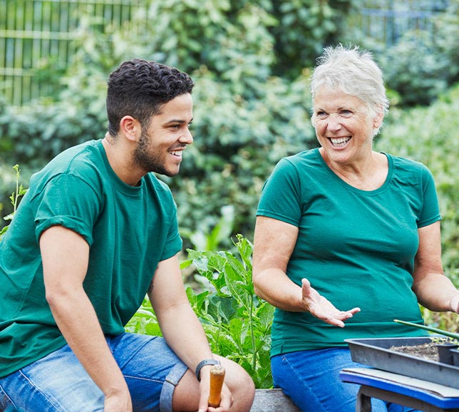 Two people sat in a garden, smiling and potting plants