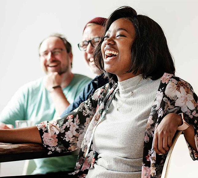 Three people sitting and laughing together, with a woman in the foreground , enjoying a light moment.