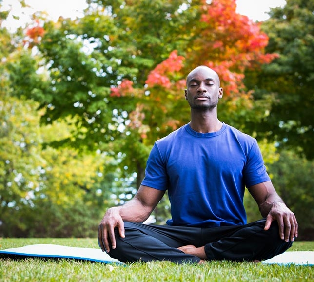 Man meditating outside on a mat surrounded by trees