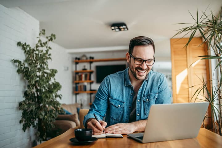 Man sat at a laptop smiling and making notes