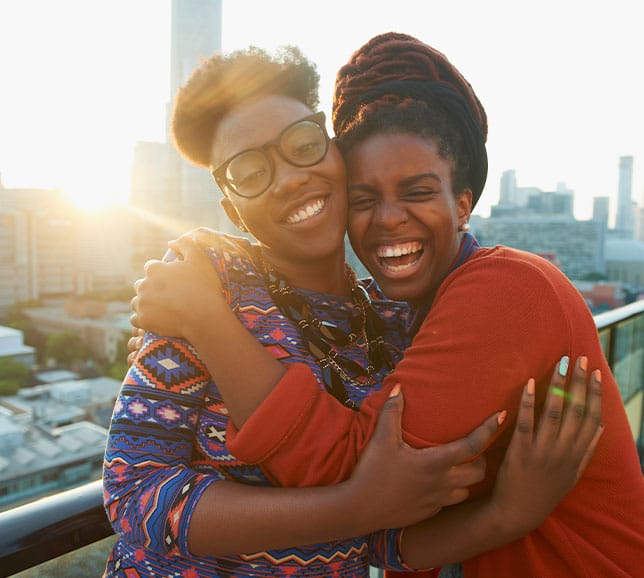 Two women standing on a balcony in the sunshine, hugging