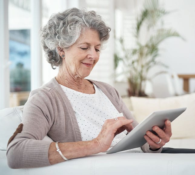 Senior woman sat on a sofa using a tablet device