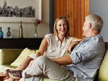 A couple sits on a green sofa in a modern living room, talking and smiling.