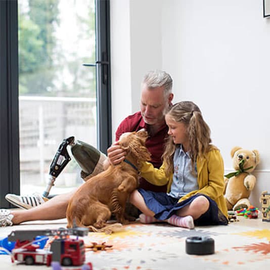 Man with prosthetic leg sat on floor with little girl and a dog