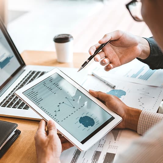 Two people discussing charts on a tablet and papers at a desk