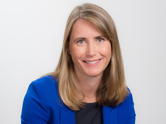 A woman with long blonde hair wearing a blue blazer smiles against a plain white background.