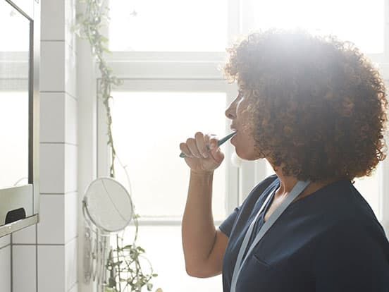 Lady with curly hair brushing teeth in mirror