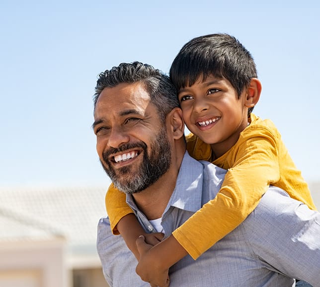 Man carrying his son on his back, both smiling in the sunshine