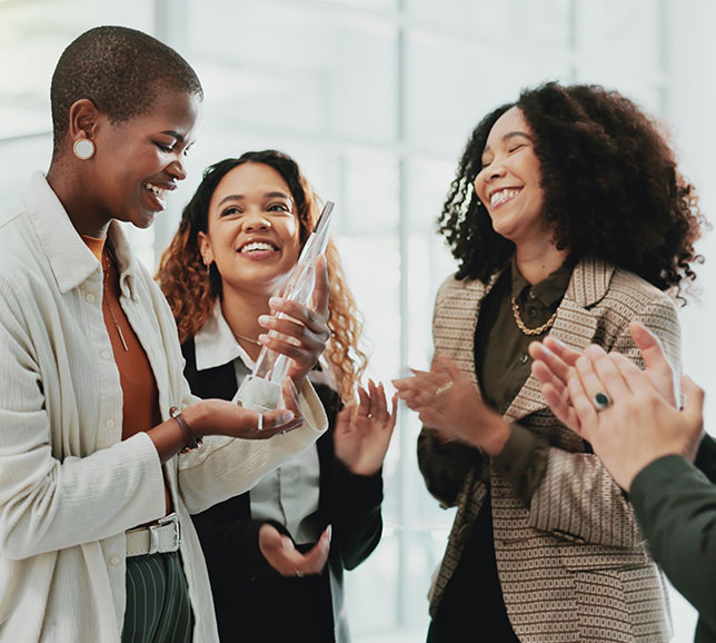 Three people celebrating as one holds an award. They are smiling and applauding, standing in a bright, modern space.