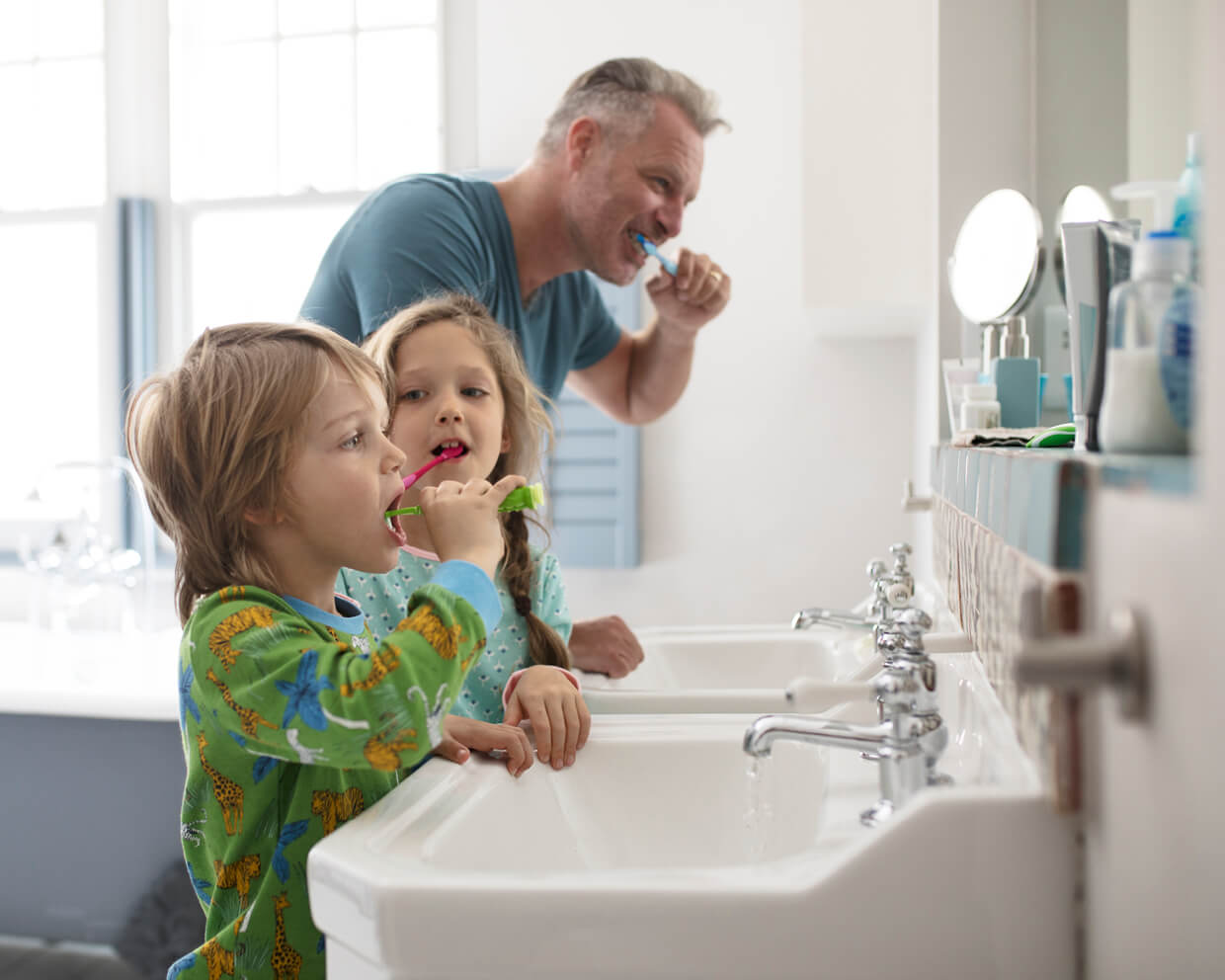 Father with young son and daughter all brushing their teeth 