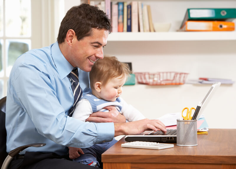 Man sat working at laptop with a toddler on his lap