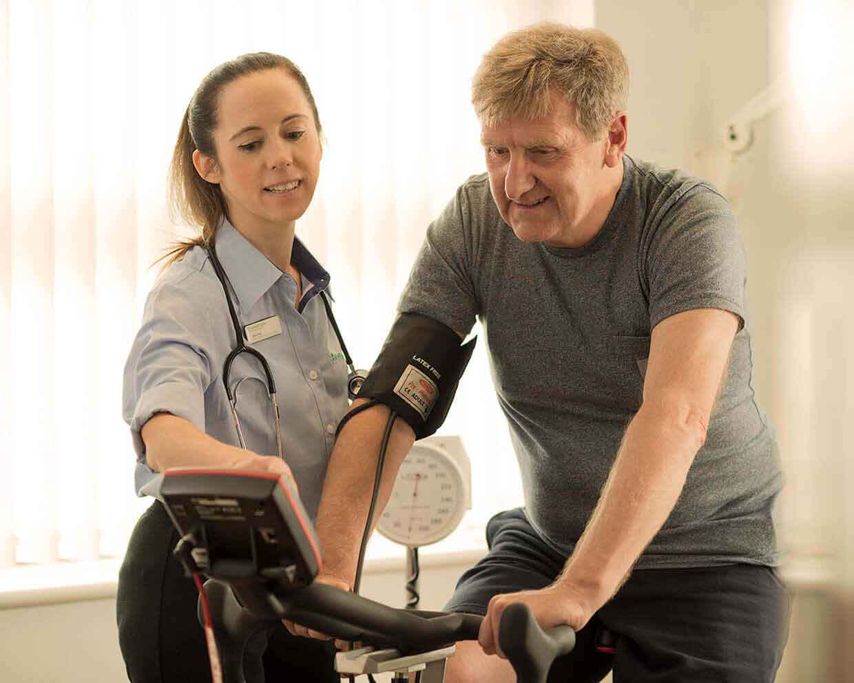 Older man on an exercise bike with health monitors attached to him