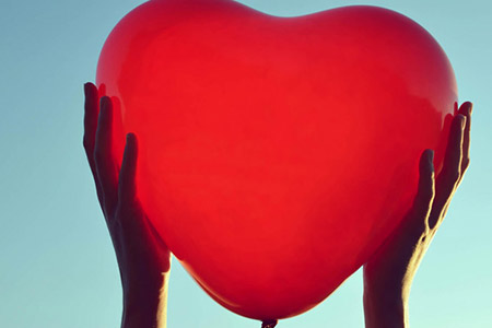 Hands holding up heart shaped balloon to the sky
