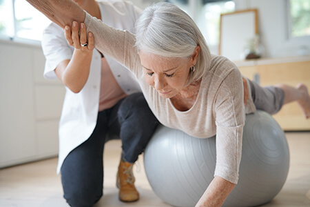 Woman stretching on exercise ball with help from physio