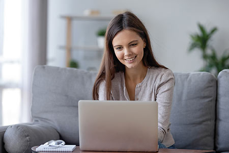 Woman smiling and working at laptop on sofa