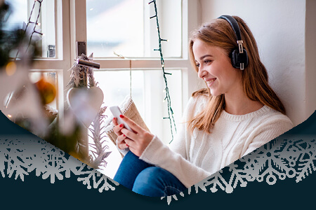 Woman sat by festive window listening to music on headphones