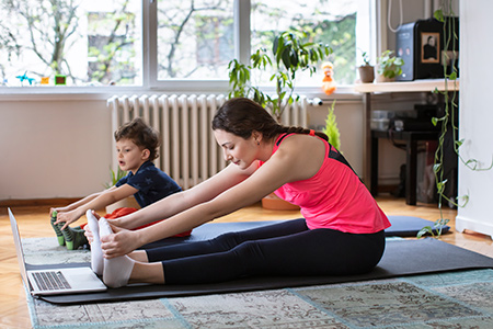 Woman and child doing yoga stretches together in front of laptop
