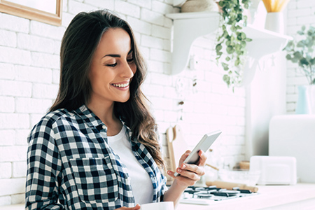 Woman using mobile phone in kitchen and smiling