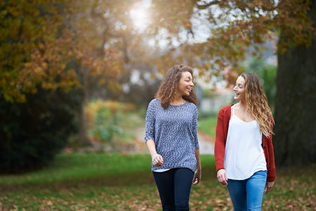Two friends smiling and walking in autumnal park