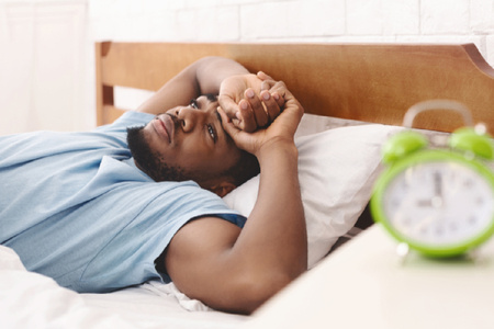 Man in bed looking worried with alarm clock