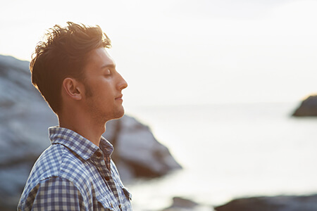 A man meditating with his eyes closed by the sea shore