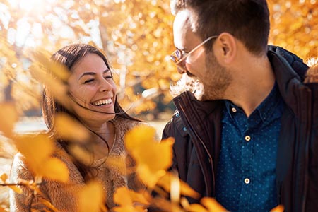 A couple smiling surrounded by golden leaves