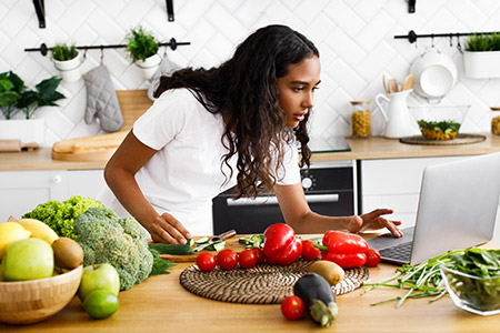 Woman preparing vegetables and following recipe on laptop