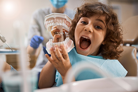 Boy opening mouth wide while holding false teeth