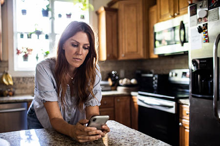 Woman leaning on kitchen counter using smart phone