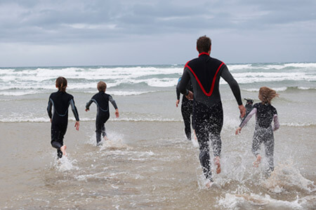 Family wearing wetsuits running into the sea waves