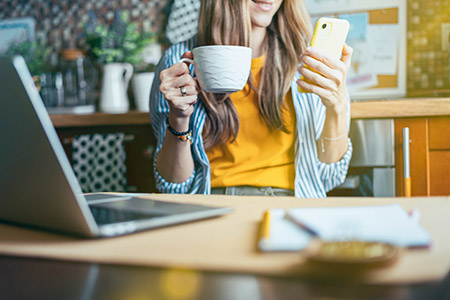 Woman working from home drinking from mug and looking at mobile phone