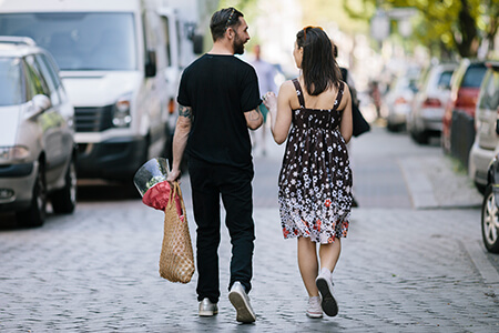 A couple talking as they walk down a street lined with parked cars
