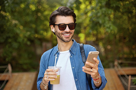 Man wearing sunglasses, holding mobile phone and a refreshing drink