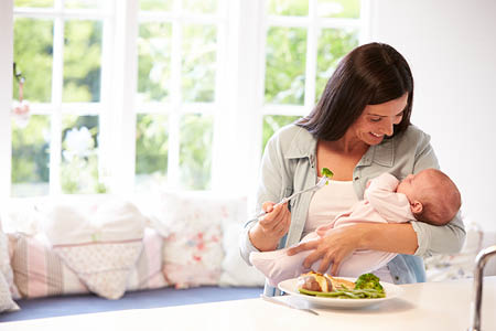 Woman smiling at baby in her arms whilst eating a salad