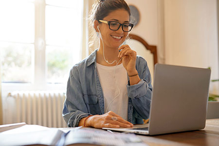 Woman working from laptop wearing earphones and smiling