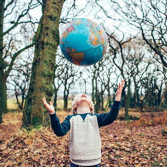 Child throwing a globe in the air surrounded by wintery trees