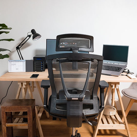 A photo of a home office with an ergonomic setup including a chair at the correct height and a laptop on a stand