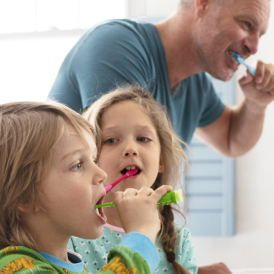 Father and young children brushing teeth together