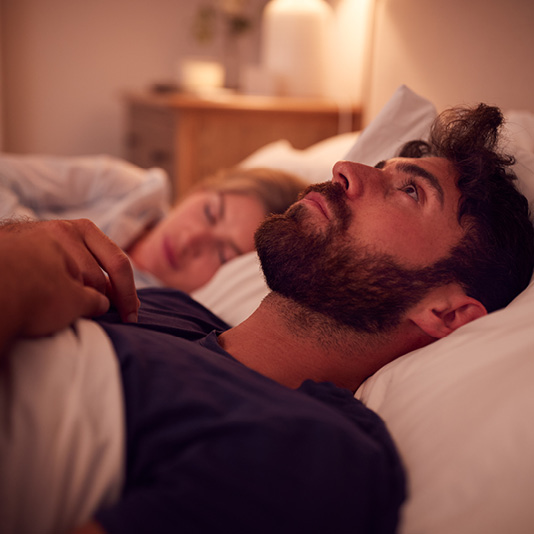 Man lying awake in bed whilst partner is asleep