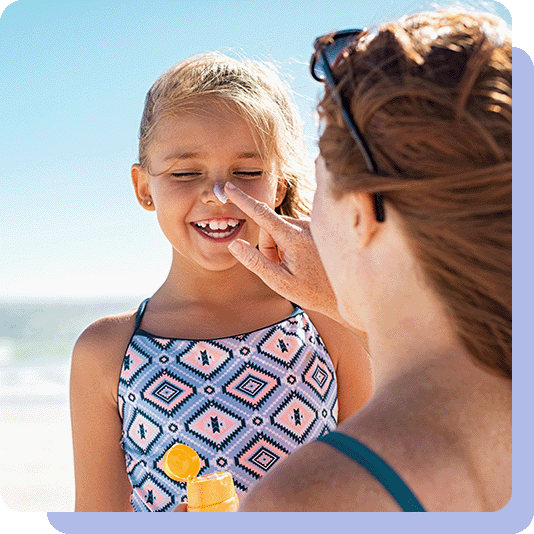 Mother putting suncream on daughters nose at the beach