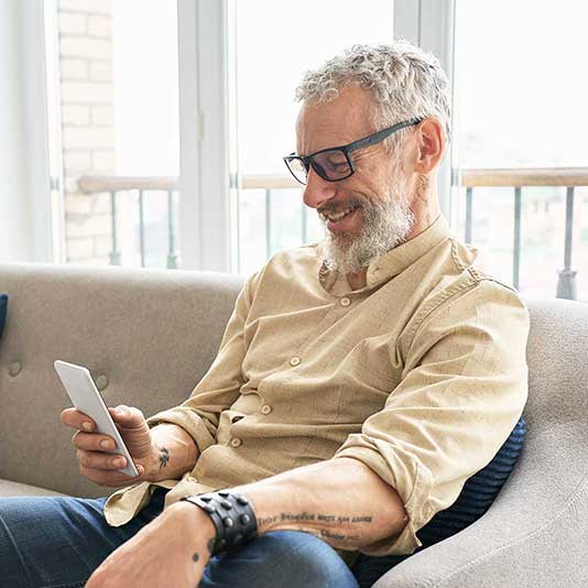 Relaxed man wearing glasses using mobile app while sat on the sofa
