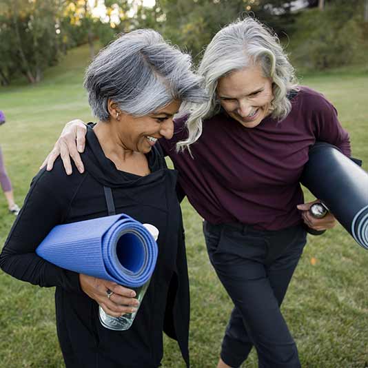 Two women with arms around each other carrying yoga mats